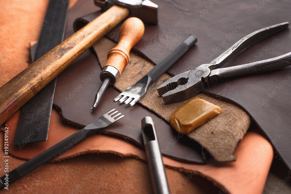 Set of leather craft tools on wooden background. Workplace for shoemaker. Piece of hide and working handmade tools on a work table.