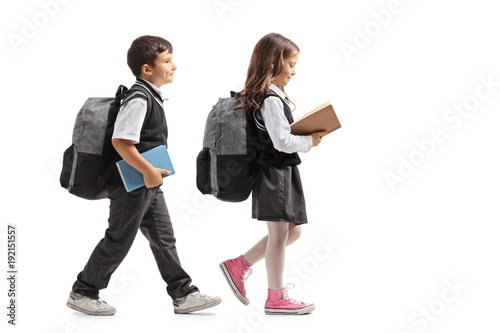 Full length profile shot a schoolboy and a schoolgirl with backpacks and books walking photo