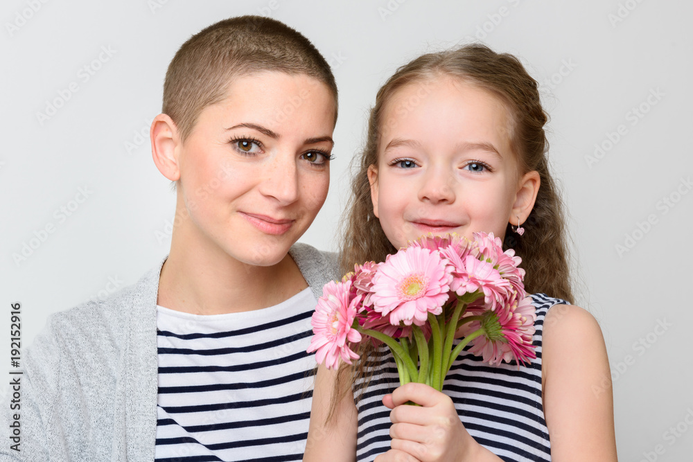 Happy Mother's Day, Women's day or Birthday background. Cute little girl giving mom, cancer survivor,  bouquet of pink gerbera daisies. Mother and daughter smiling and looking at camera.