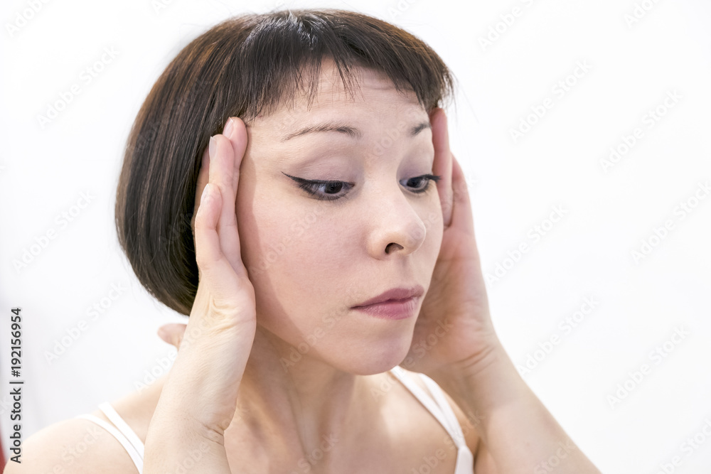 A young woman checking wrinkles on her forehead. Horrified young woman looking in the bathroom mirror staring open mouthed a first sign of ageing A young woman checking wrinkles on her forehead. Horrified young woman looking in the bathroom mirror staring open mouthed a first sign of ageing
