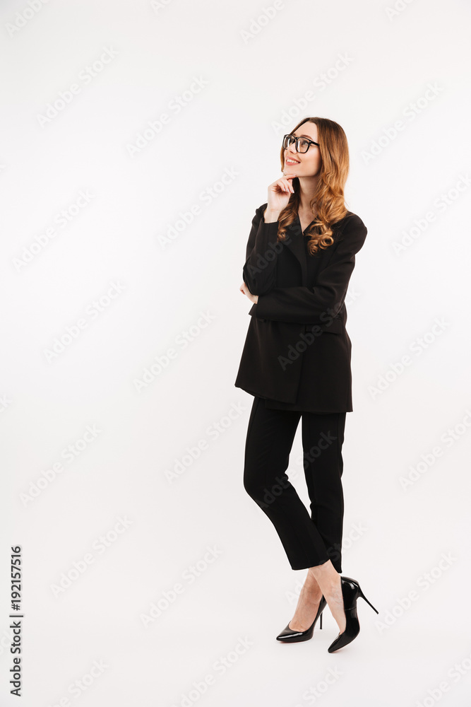 Full-length businesslike woman in total black outfit and eyeglasses smiling and looking upward on copyspace, isolated over white background Full-length businesslike woman in total black outfit and eyeglasses smiling and looking upward on copyspace, isolated over white background