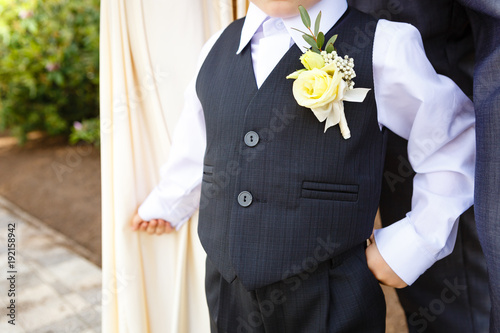 Little boy dressed in suit with boutonniere standing at sunny day outdoor