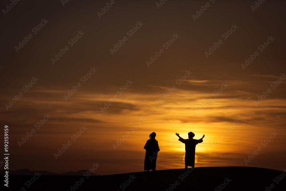 Silhouette of two berber in desert Sahara, Morocco with beautiful and colorful sunset  in background