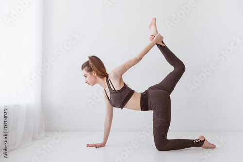 Fit young Caucasian woman practicing yoga at home standing in cat and cow pose arching her back. Raise your leg above your head. Lifestyle. photo