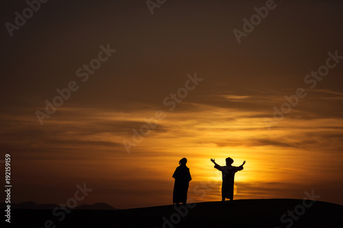 Silhouette of two berber in desert Sahara, Morocco with beautiful and colorful sunset in background