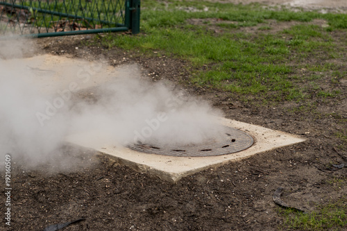 Hot white steam coming out of metal manhole or metal hatch