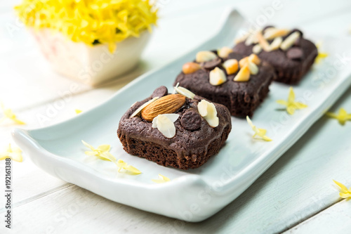 Brownie cake with almond on top with yellow flower in the background