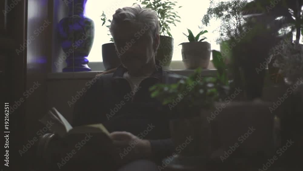 Elderly man is reading a book in a room with video flowers Elderly man is reading a book in a room with video flowers
