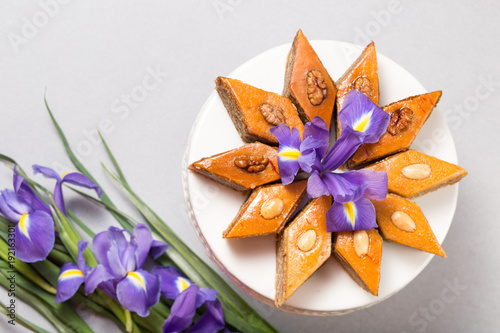 Novruz Azerbaijan spring celebration plate with traditional national sweet pastries pakhlava with walnuts and honey decorated with spring flowers purple fleur de lys on grey background copy space