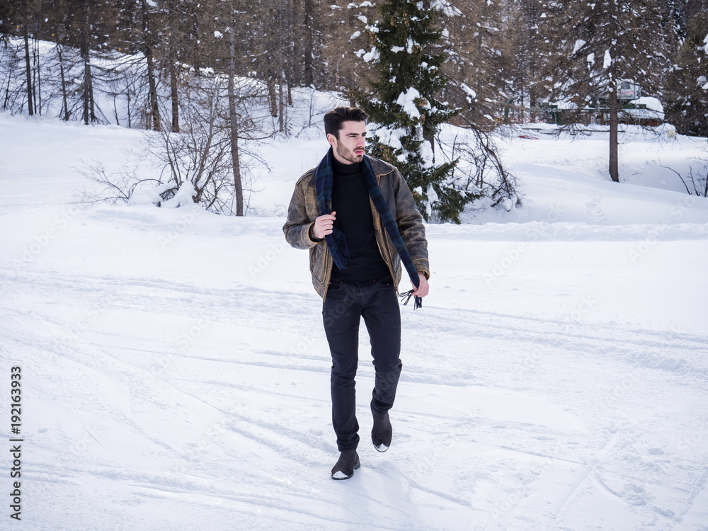 Stylish man walking confidently looking away on territory of contemporary winter resort covered in snow in the mountain Stylish man walking confidently looking away on territory of contemporary winter resort covered in snow in the mountain
