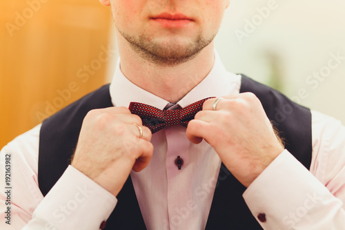 A man in a suit with both hands adjusts the butterfly. The bridegroom at the wedding