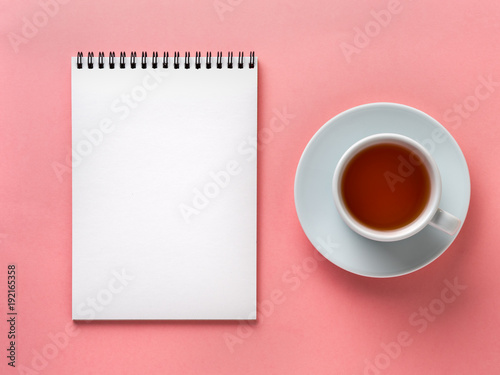 Blank notepad white page  and cup of tea on pink desk, color background. Top view,  flat lay.