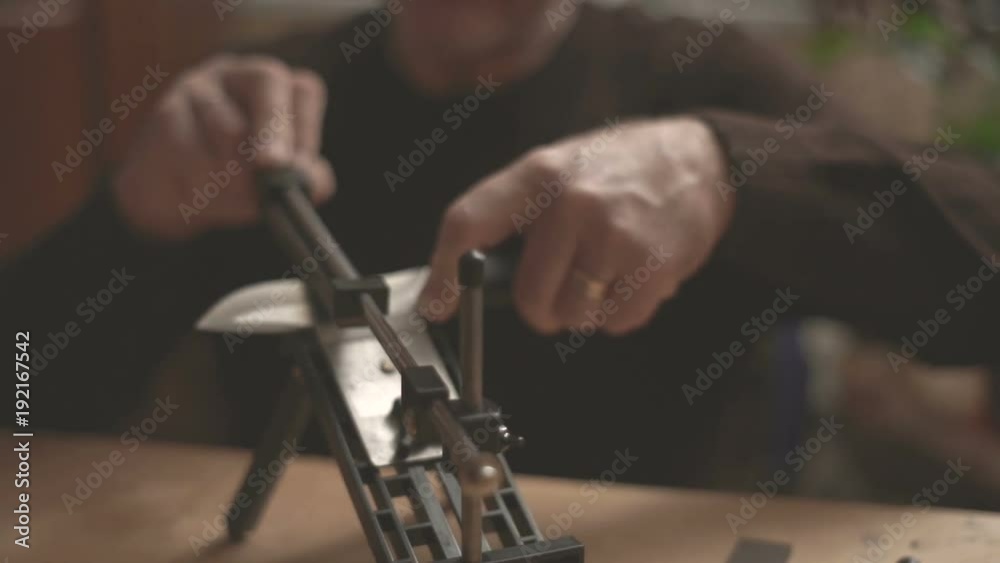 Man sharpening a knife sitting at a table in front of a video window Man sharpening a knife sitting at a table in front of a video window
