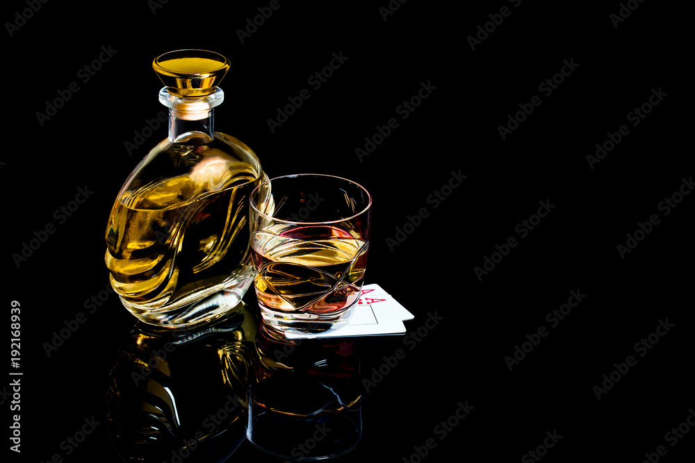 Decanter and glass of brandy with playing cards on black background