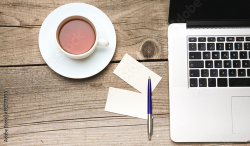 Blank business cards with pen, laptop and tea cup on wooden office table