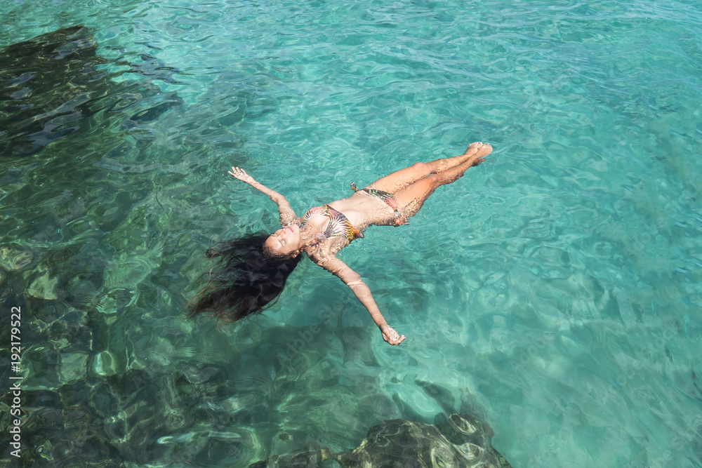 Attractive Mixed Race Woman in Bikini Lying on Clear Blue Water at Tropical Island Beach.