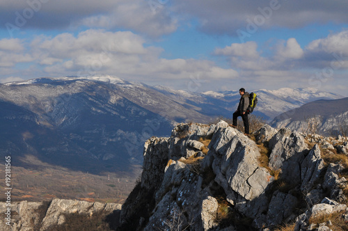 Young man on a cliff edge on the top of mountain with gorgeous view. Hiker on mountain peak on beautiful sunny day