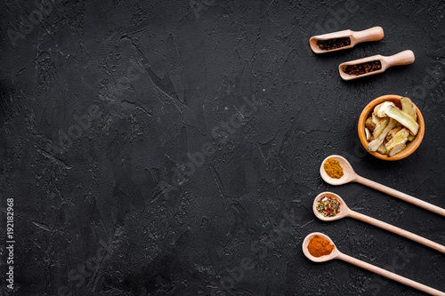 Condiments, seasoning and spices concept. Dry spices in wooden spoons near sliced ginger on black background top view copy space