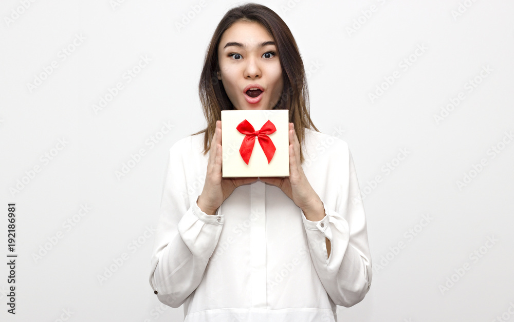 Indoor portrait of wondered young woman holds gift box with red ribbon close up on the white background. Holiday present concept. Selective focus and shallow DOF Indoor portrait of wondered young woman holds gift box with red ribbon close up on the white background. Holiday present concept. Selective focus and shallow DOF