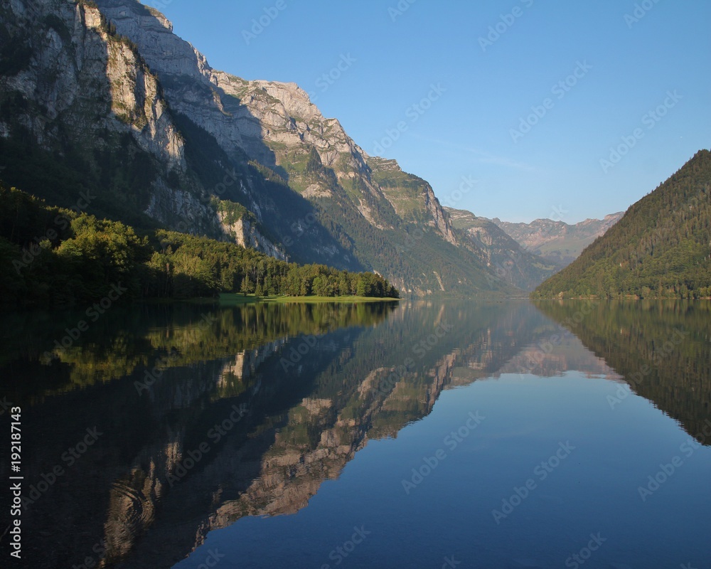 Summer morning at lake Klontalersee, Switzerland. Mountain range mirroring on the surface.