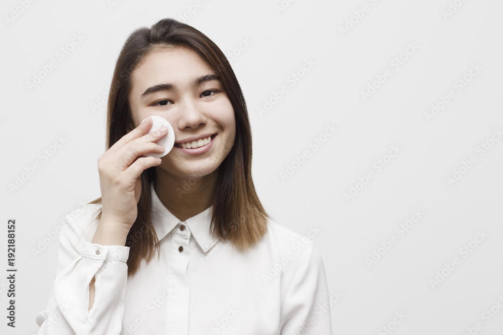 Young attractive woman removing makeup with cotton swab pad from face. Happy smiling girl taking care of skin. Healthcare and skincare concept Young attractive woman removing makeup with cotton swab pad from face. Happy smiling girl taking care of skin. Healthcare and skincare concept