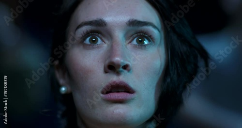 Close up of a scared woman who jumps with fear while watching a scary movie