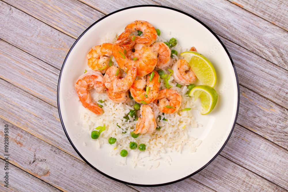 Shrimps with ginger rice and green peas, lime on white plate on wooden background