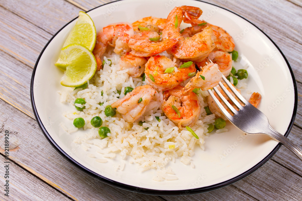 Shrimps with ginger rice and green peas, lime on white plate on wooden background Shrimps with ginger rice and green peas, lime on white plate on wooden background