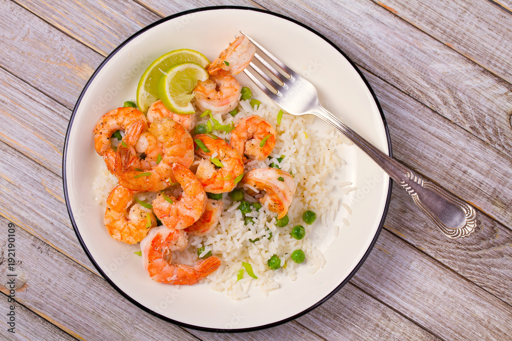 Shrimps with ginger rice and green peas, lime on white plate on wooden background
