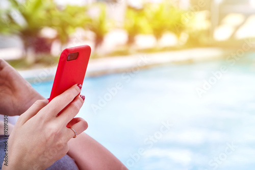 girl on a lounger near the swimming pool with modern mobile phone (smartphone) in her hands (with copy space)