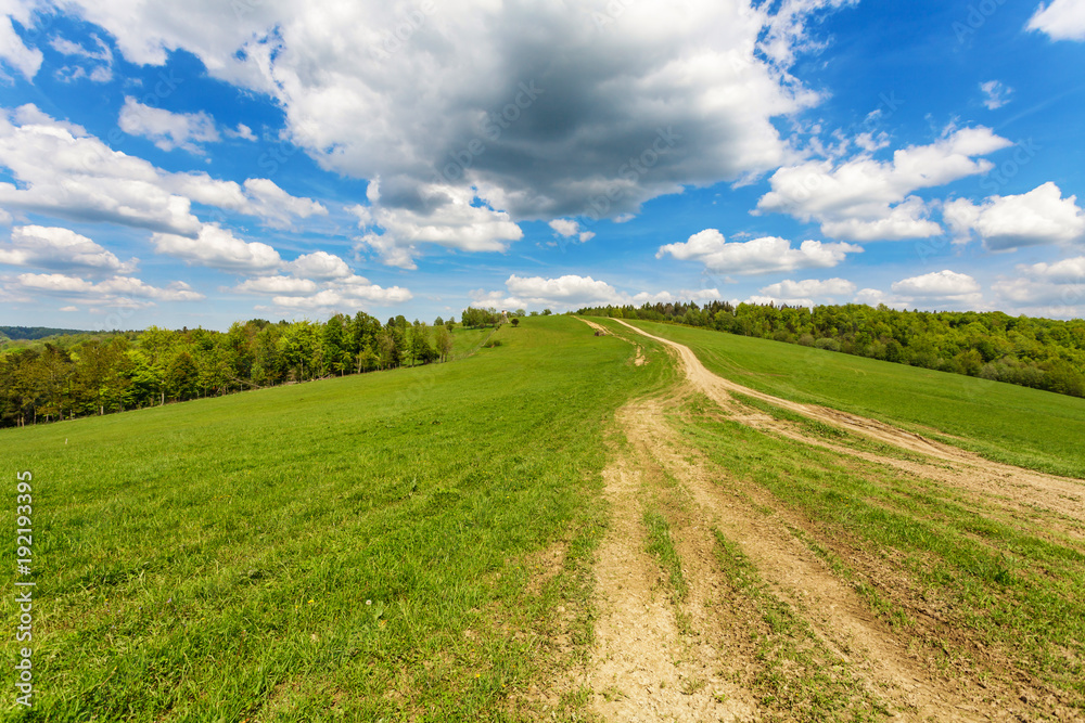 Blue cloudy sky over green hills and country road Blue cloudy sky over green hills and country road