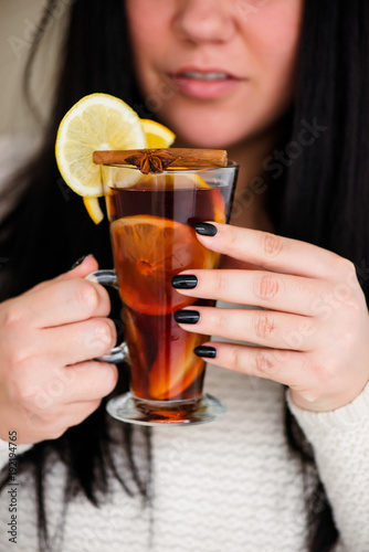 a glass cup with mulled wine with a piece of orange and an anise star in his hands in a warm sweater. Close-up