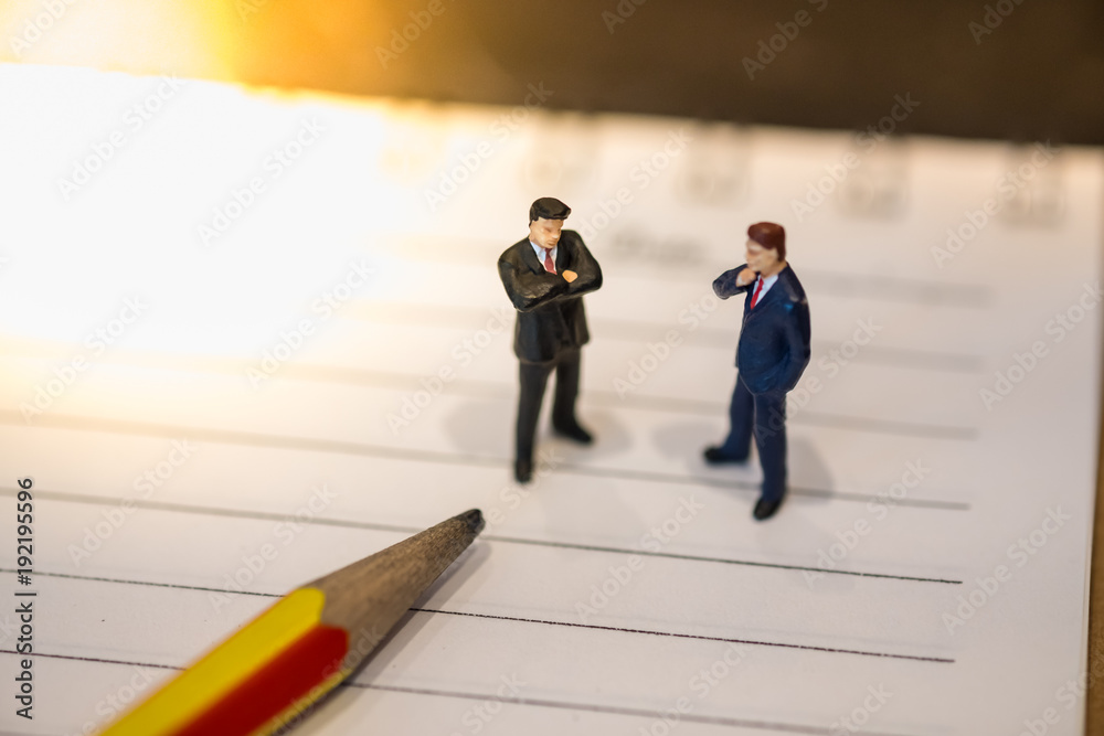 Business and planning concept. Two businessman miniature figures standing on notebook with pencil.