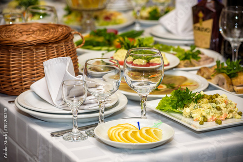 Glasses, forks, knives, napkins and decorative flower on a table served for dinner in cozy restaurant.