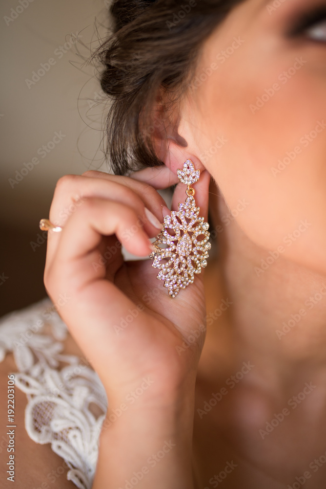 Bride puts on a gold earring in her ear. Delicate brunette touches her luxury earrings. Wedding details