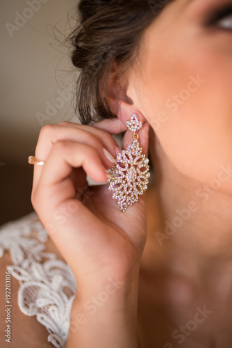 Bride puts on a gold earring in her ear. Delicate brunette touches her luxury earrings. Wedding details