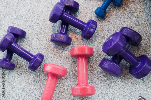 Purple and pink dumbbells lie on the gray floor at gym photo