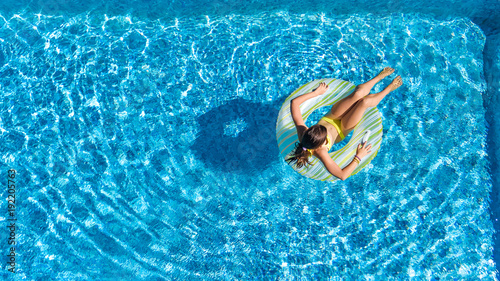 Aerial top view of little girl in swimming pool from above, kid swims on inflatable ring donut , child has fun in water on family vacation resort 