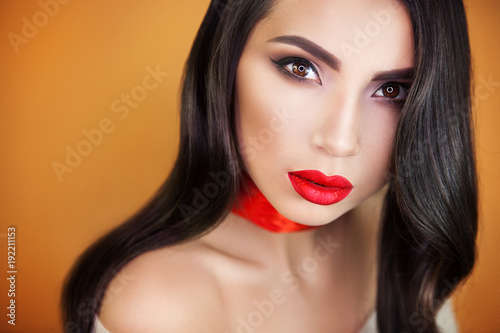 a beautiful girl with sensual bright red lips on an orange background, a red ribbon on her throat does not leave anyone indifferent, everyone looking into her brown eyes.