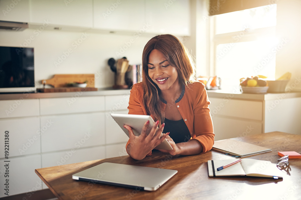 Obraz premium Smiling young female entrepreneur using a tablet in her kitchen