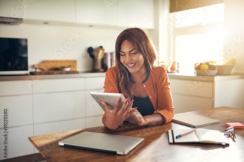 Smiling young female entrepreneur using a tablet in her kitchen photo