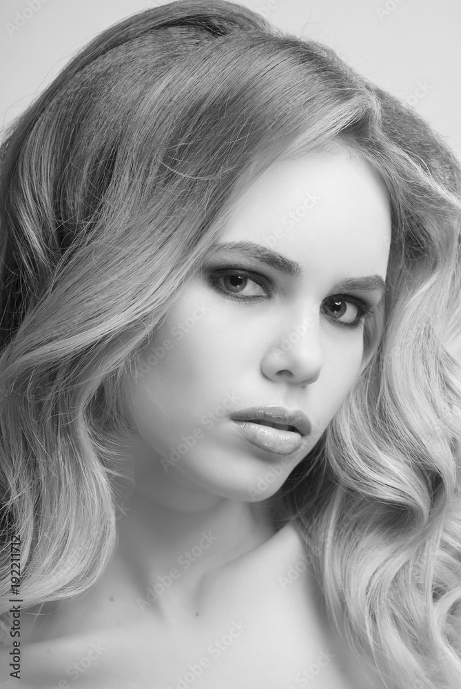 Portrait of blonde girl with makeup and hairstyle from curly hair on grey background close-up black and white image. Portrait of blonde girl with makeup and hairstyle from curly hair on grey background close-up black and white image.