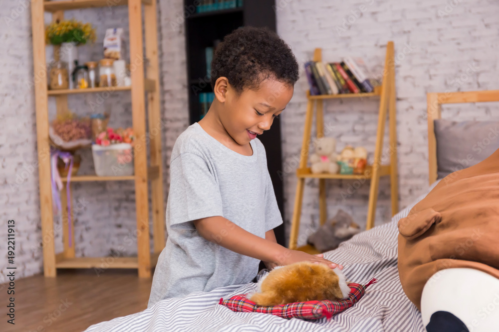 Fototapeta premium Young African American boy smiling and happily playing with sleeping puppy dog at home.