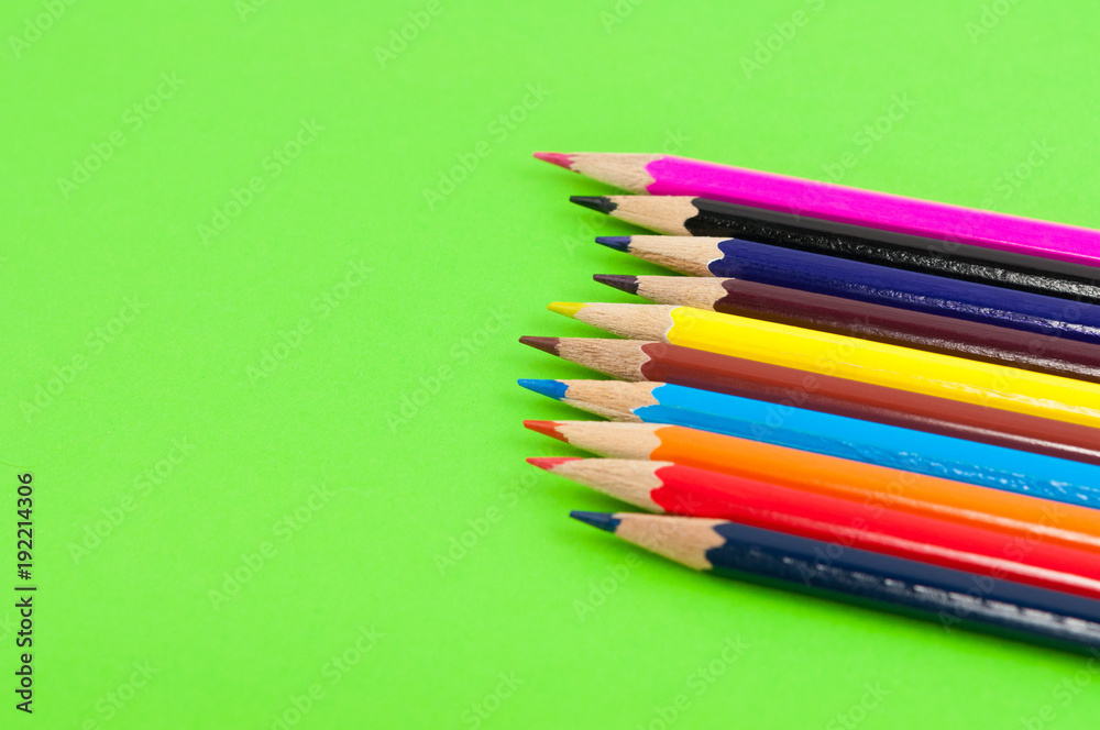 Row of colorful wooden pencils on background of green paper