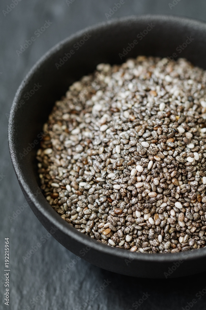 Chia seeds in a black metal bowl on a black textured board. Macro photography. Chia seeds in a black metal bowl on a black textured board. Macro photography.
