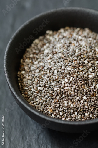 Chia seeds in a black metal bowl on a black textured board. Macro photography.