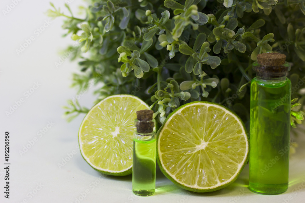 Lime oil skin and hair care home spa. Bottle of oil, green leaves. White board background Lime oil skin and hair care home spa. Bottle of oil, green leaves. White board background