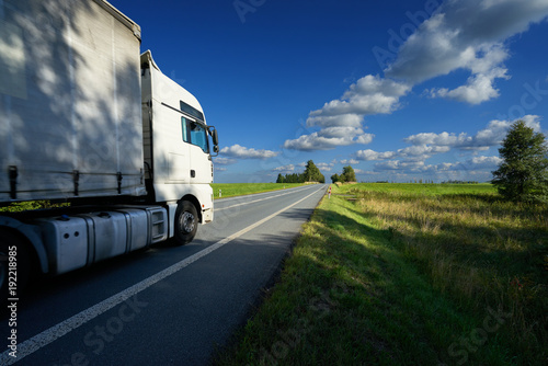 Obraz na płótnie White truck driving on the asphalt road in the countryside on a sunny day with blue sky and white clouds w salonie