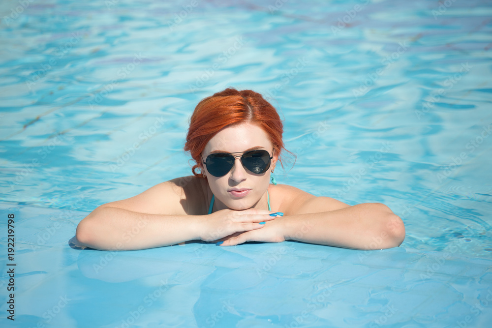 Portrait of a beautiful woman getting out of a swimming pool. beautiful long hair tanned model posing by blue pool water. Outdoor summer portrait of sexy girl in sunglasses. woman in red swimsuit.