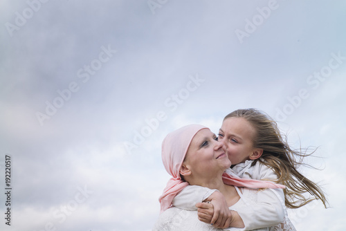 A woman with cancer is  next to her daughter. A girl is hugging a woman happy